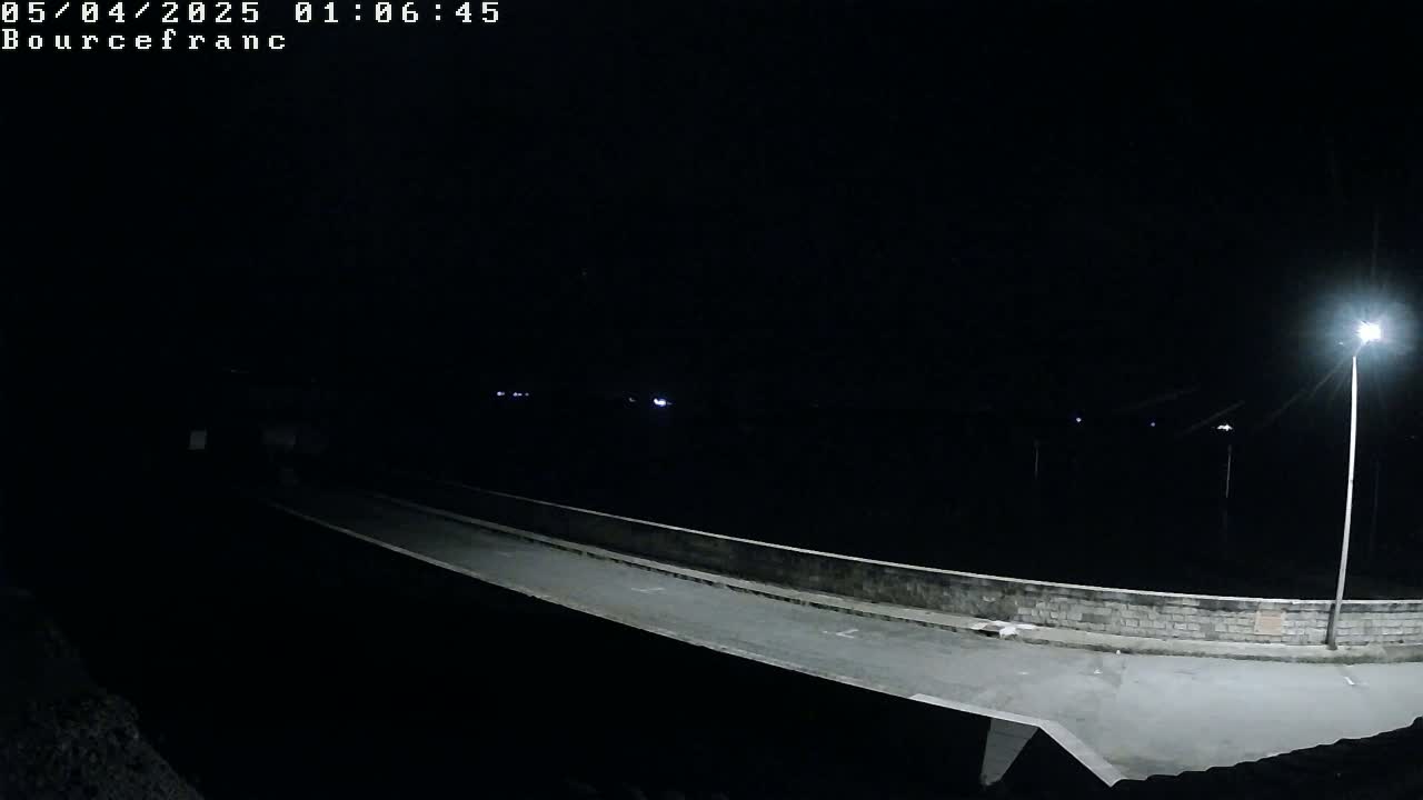 A low-light nighttime image shows an empty road or bridge lit by a few streetlights.