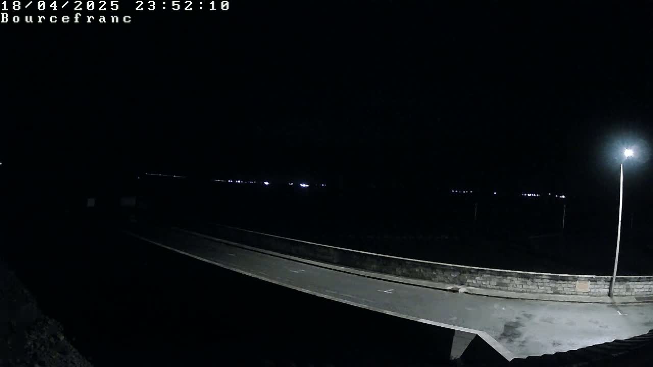 A nighttime view shows a paved road and bridge, illuminated by a single streetlight, with distant lights faintly visible in the darkness.
