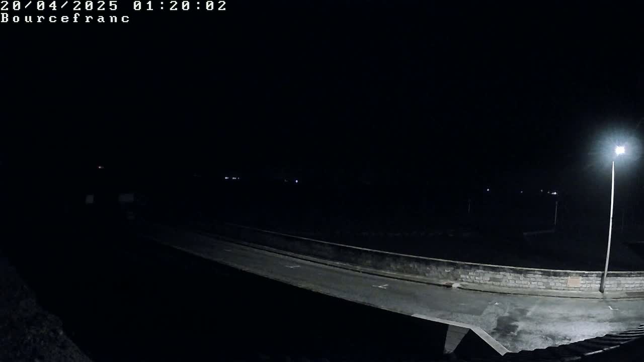 A nighttime view of a dark, empty road illuminated by a single streetlight, bordered by a low stone wall.