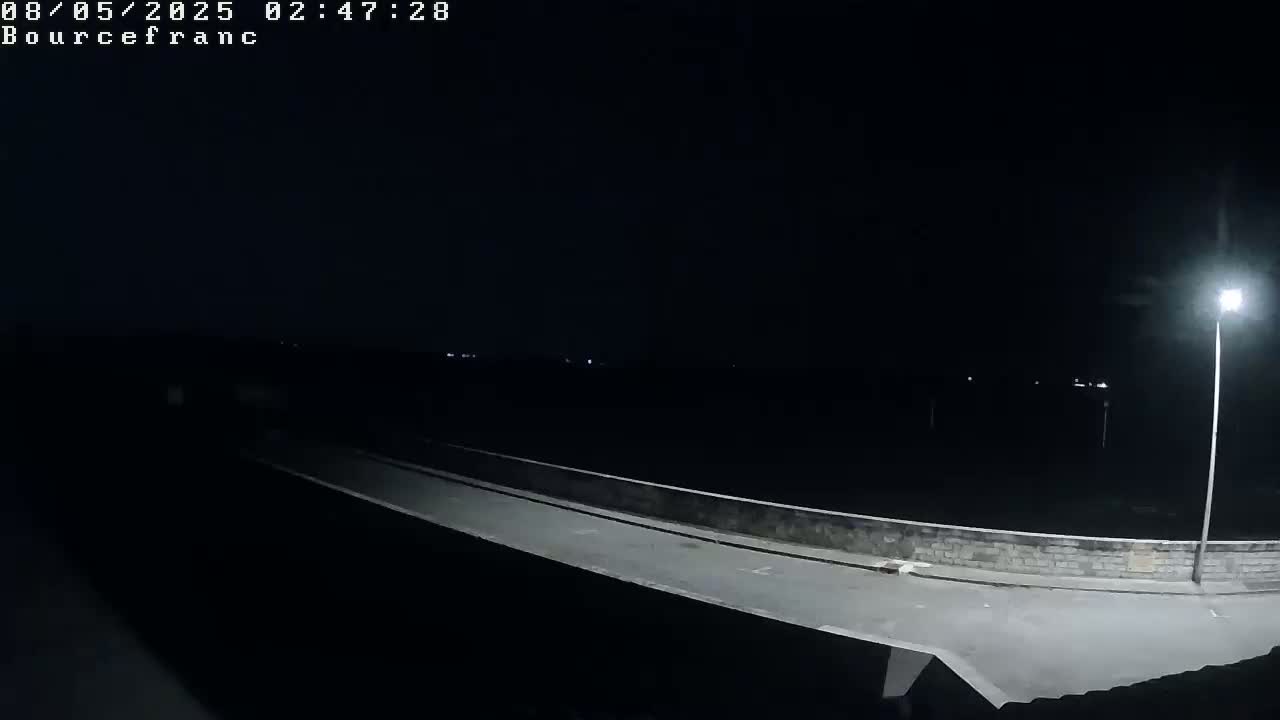 A nighttime, low-angle view shows a dark empty road on a bridge illuminated by a single streetlight.