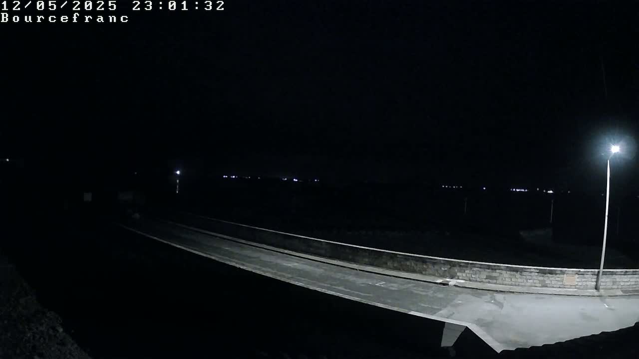 A nighttime view of a dark roadway with low-light illumination, extending to a distant horizon where faint lights are visible.