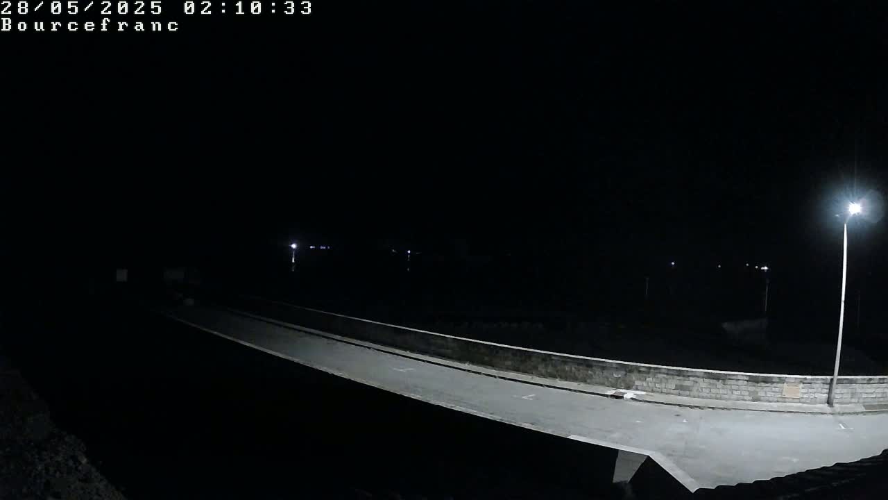 A nighttime view of a dimly lit roadway spanning a low wall, with a single streetlight illuminating a section of the scene.