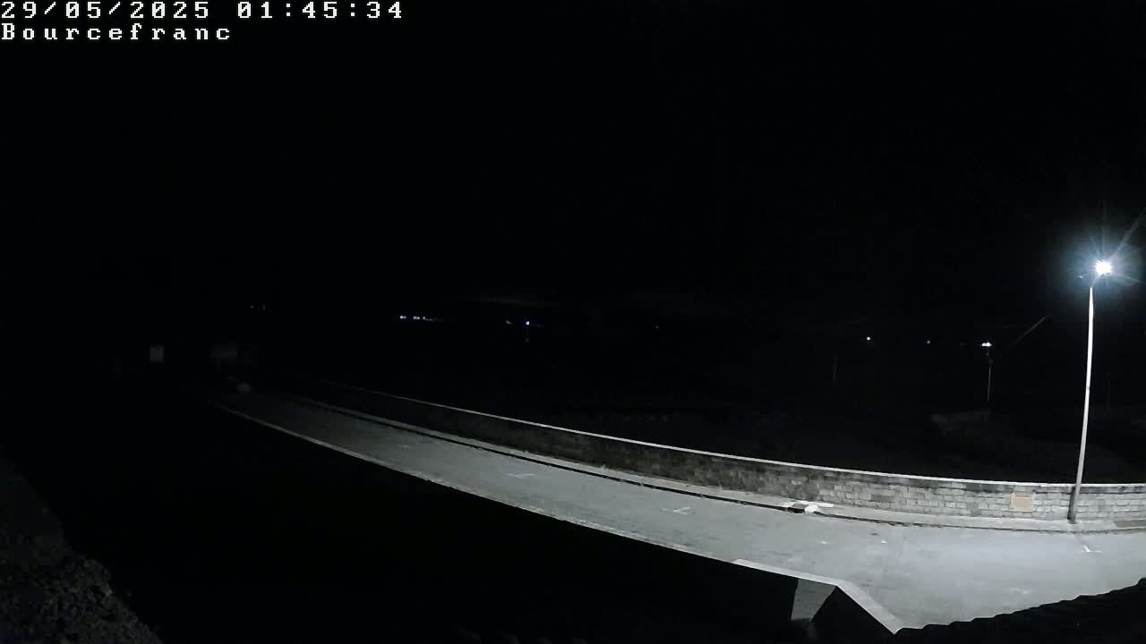 A nighttime view of a paved road and low wall illuminated by streetlights.