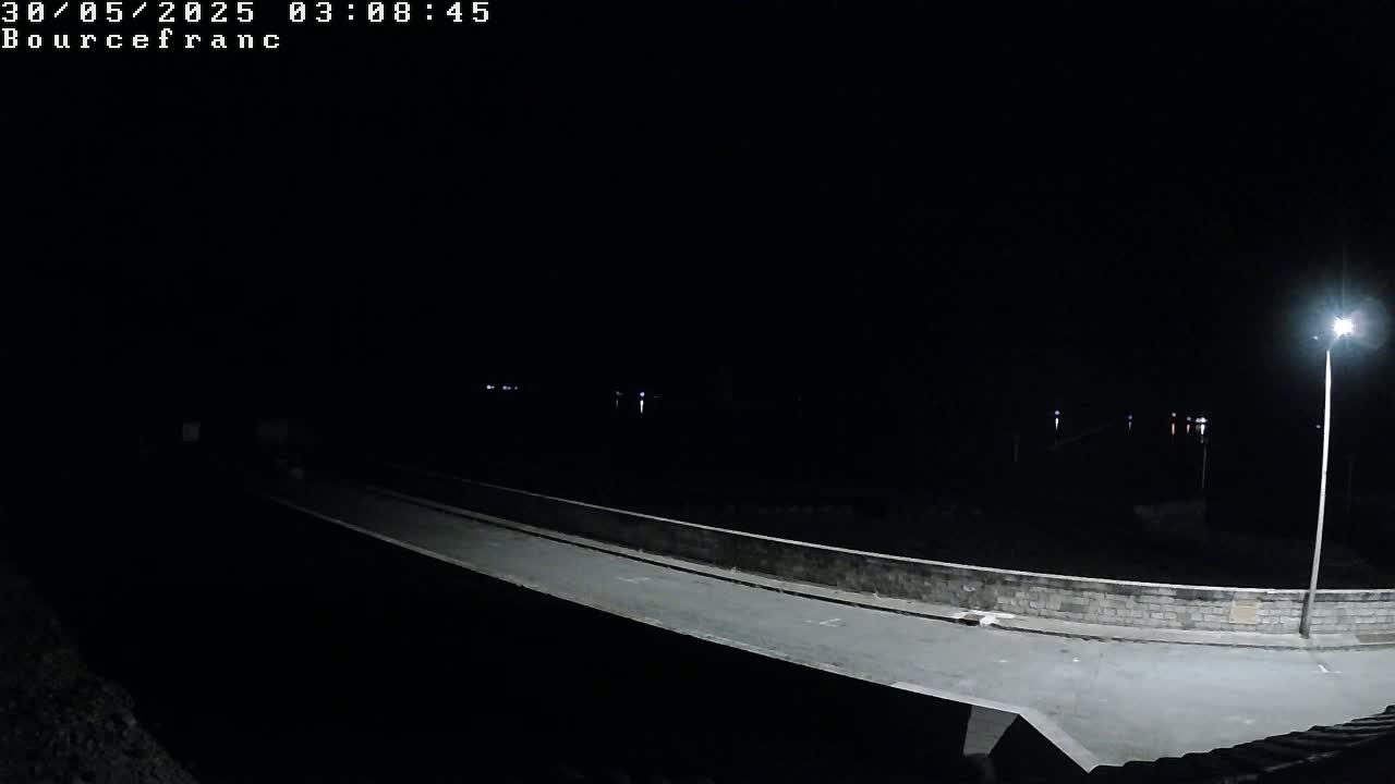 A nighttime view of a dimly lit road on a bridge, with a single lamp illuminating a section of the roadway.