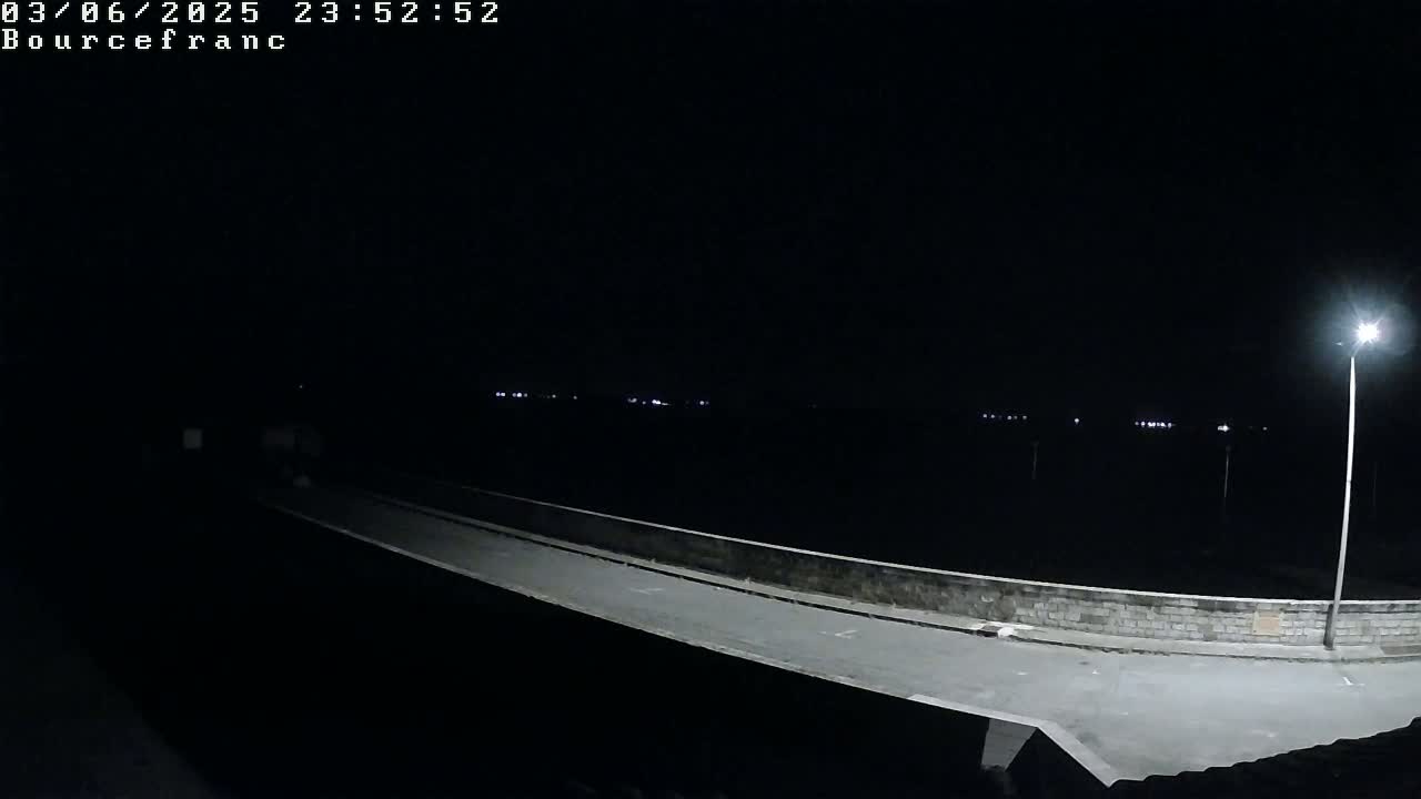A nighttime view of a dimly lit road and wall, extending into the dark distance where faint lights are visible.