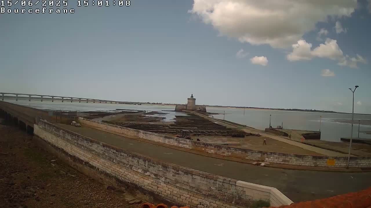 A stone tower sits on a peninsula, with a bridge visible in the distance under a partly cloudy sky.