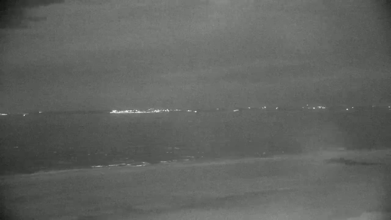 A dark, nighttime view shows a body of water with a distant line of lights on the horizon.