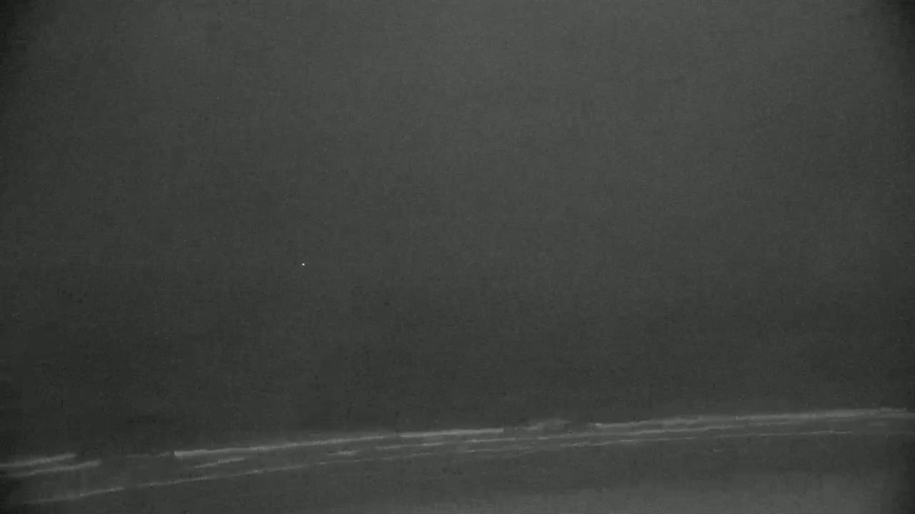 A dark, overcast sky hangs over a dimly lit ocean shoreline with small waves.