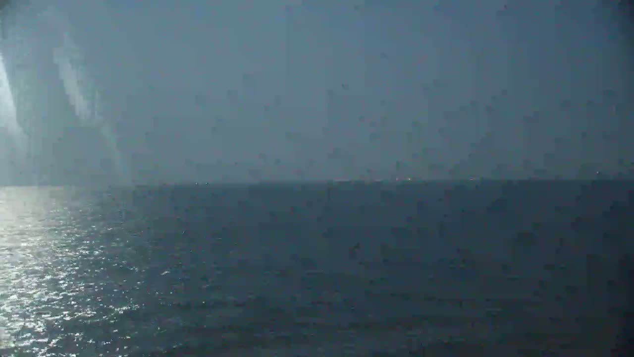 A mostly overcast sky hangs over a dark, relatively calm sea, with a distant, barely visible shoreline.