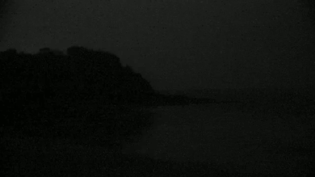 A dark, possibly nighttime, landscape shows a silhouetted hill or mountain range against a very dark sky.