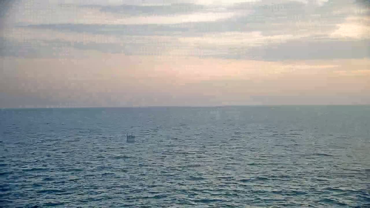 A calm ocean under a pale, cloudy sky shows a single small object floating on the water.