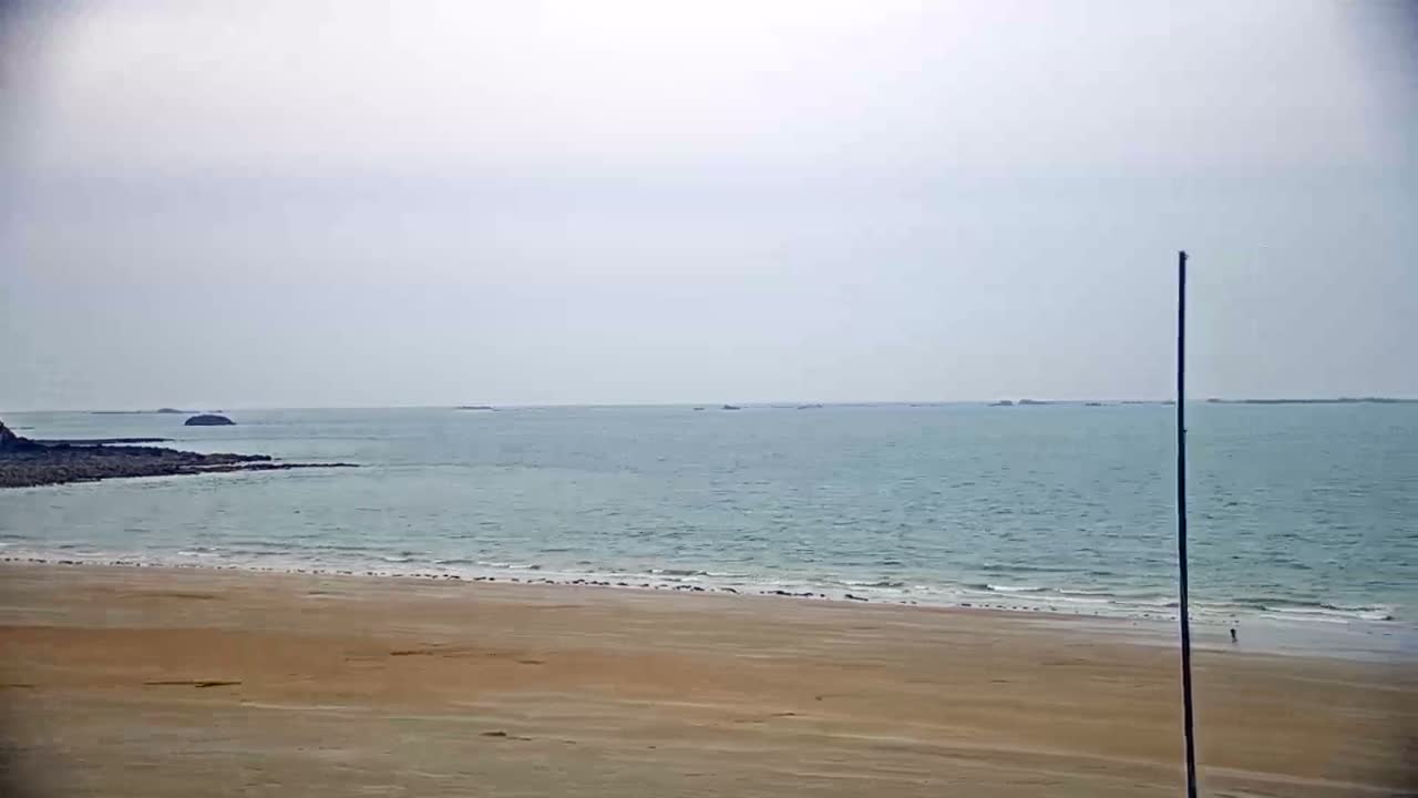 A wide sandy beach stretches to a calm sea under an overcast sky.