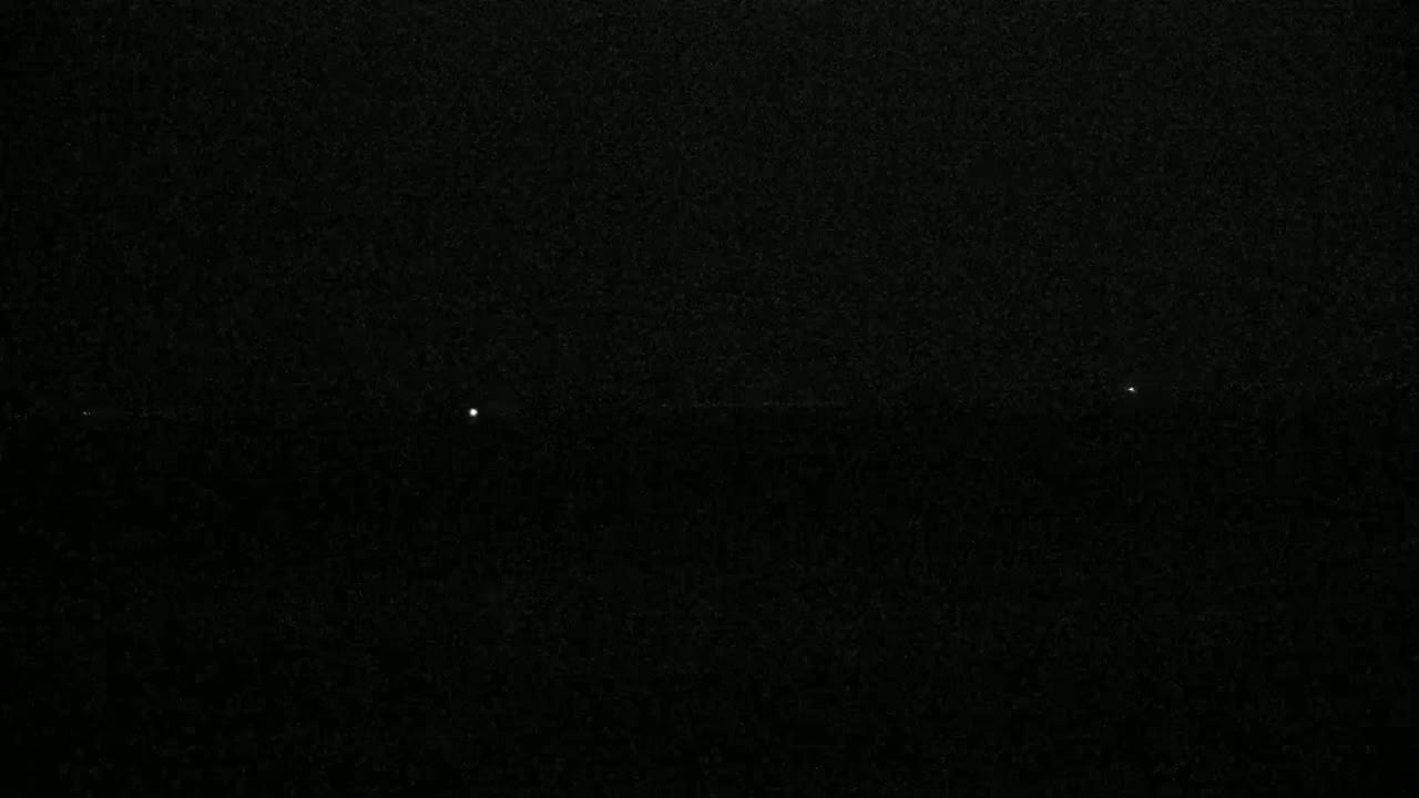 A dark, nighttime scene shows three small, bright lights in a horizontal line against a grainy black background.