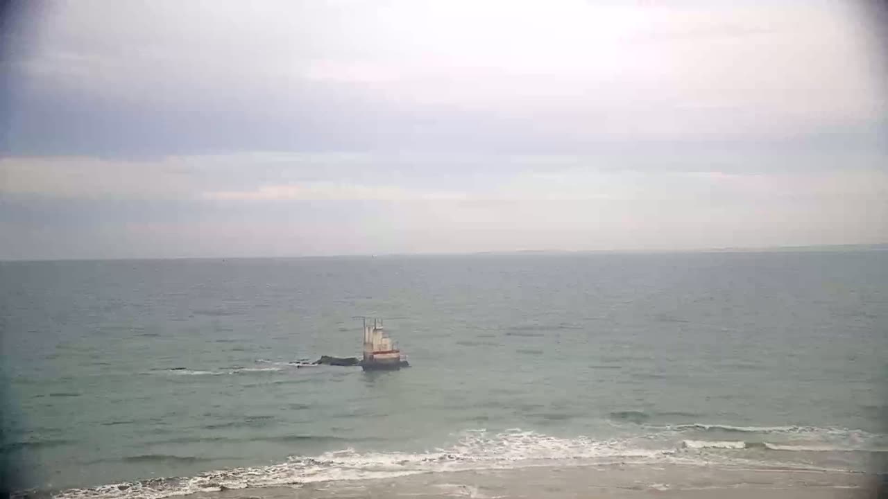 A small structure sits in the ocean near a sandy beach under an overcast sky.