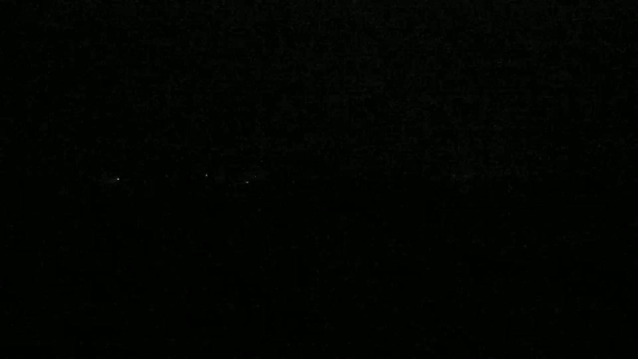 A nighttime, dark image shows a few faint lights in the distance.