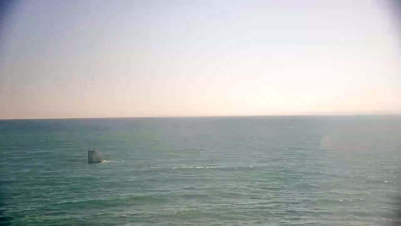 A small, light-colored vessel is visible on a calm, teal ocean under a clear, bright sky.