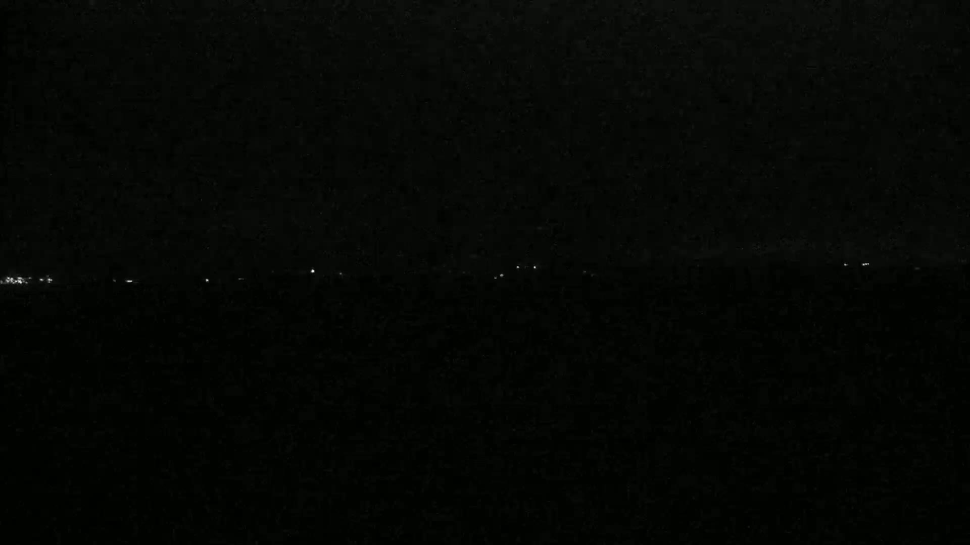 A dark, nighttime landscape shows a distant line of faint lights on the horizon.