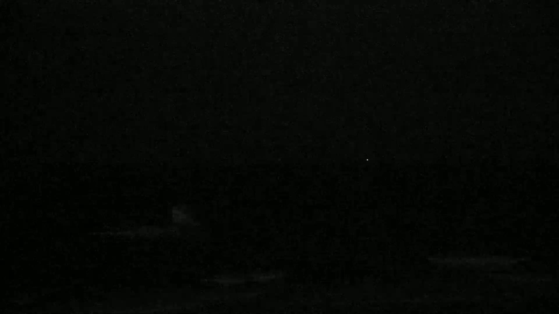 A very dark, nighttime scene shows a faint, blurry light in the distance.