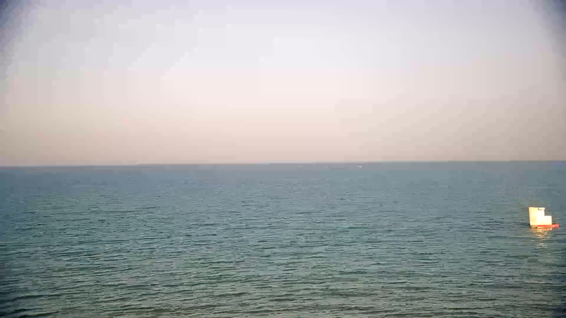 A small sailboat is visible on a calm, hazy ocean.