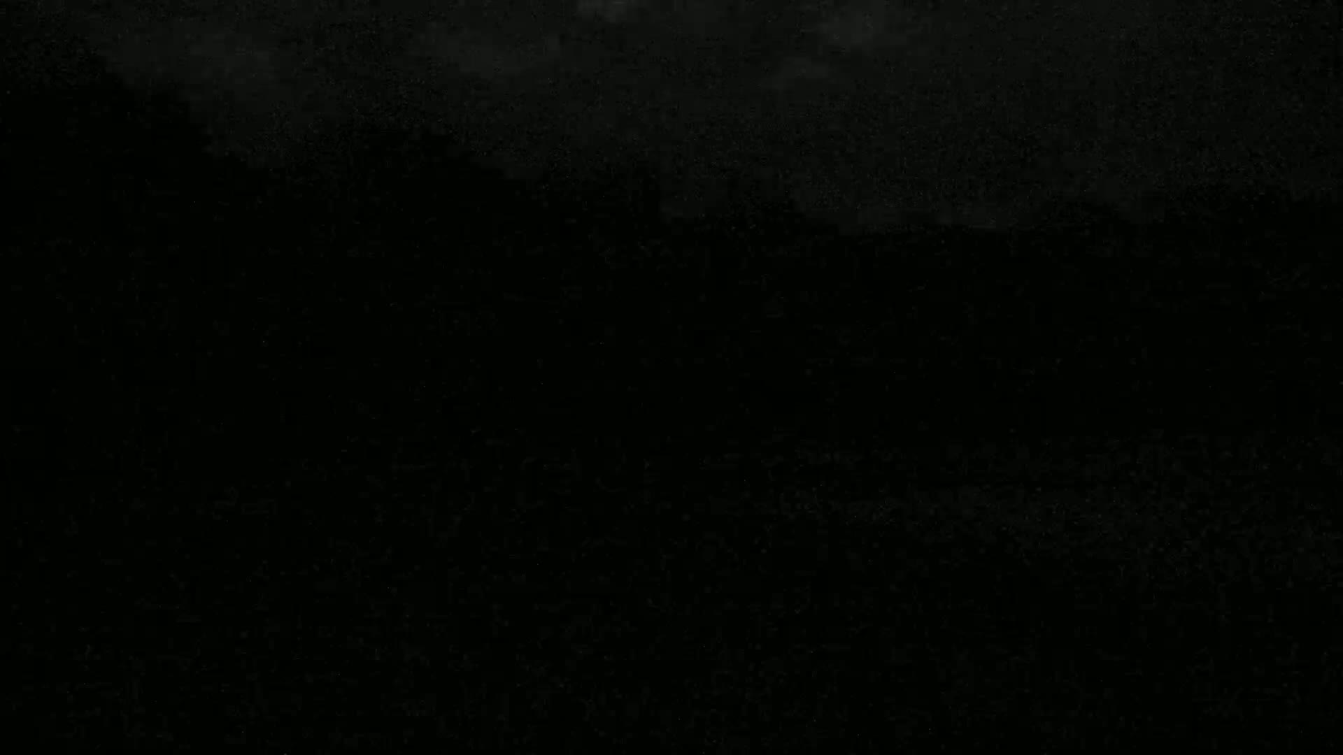 A dark, mostly black image with a slightly lighter, speckled area at the top that could possibly be a night sky.
