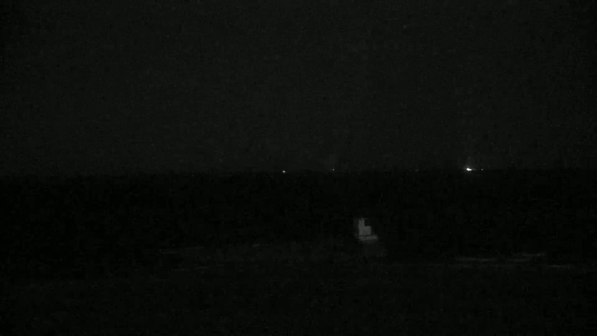 A dark, nighttime scene shows a body of water with a few faint lights visible in the distance.