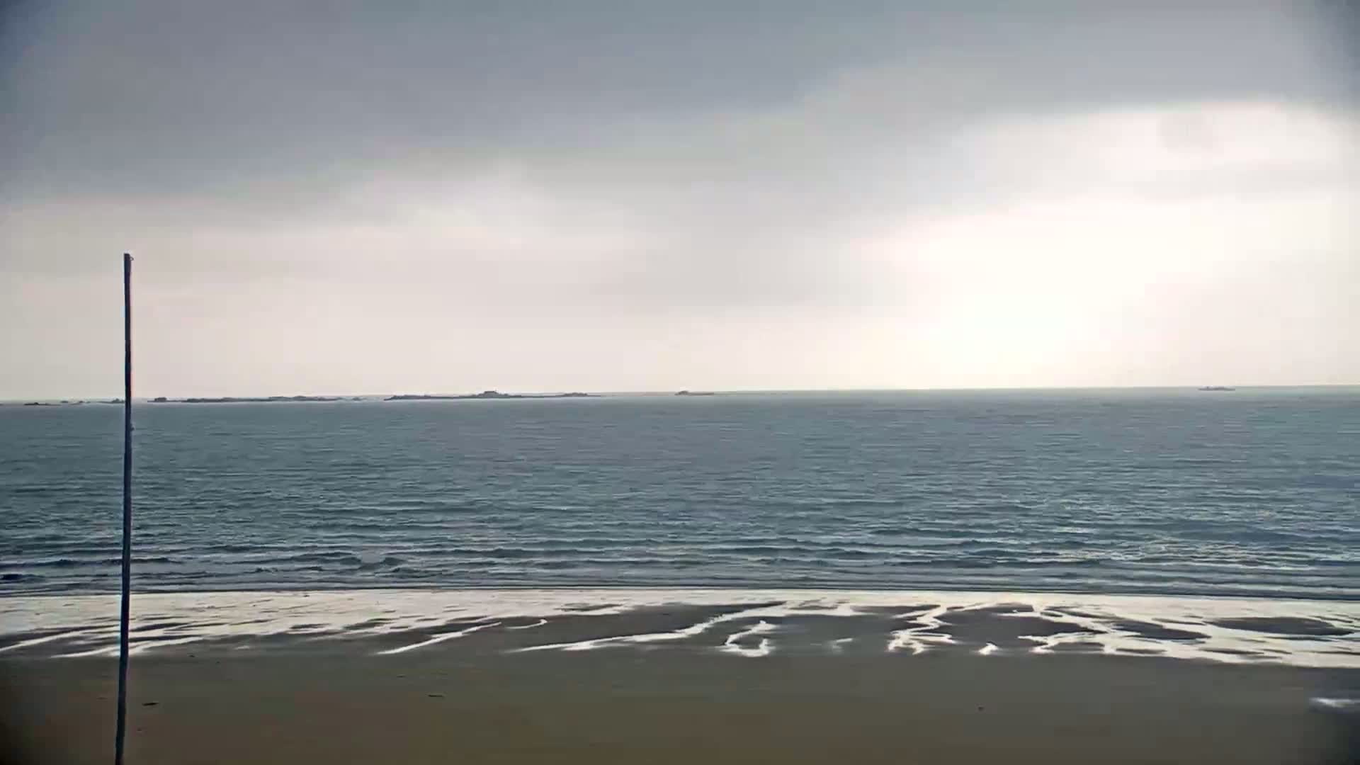 A sandy beach stretches to a calm, gray sea under an overcast sky, with distant landmasses visible on the horizon.