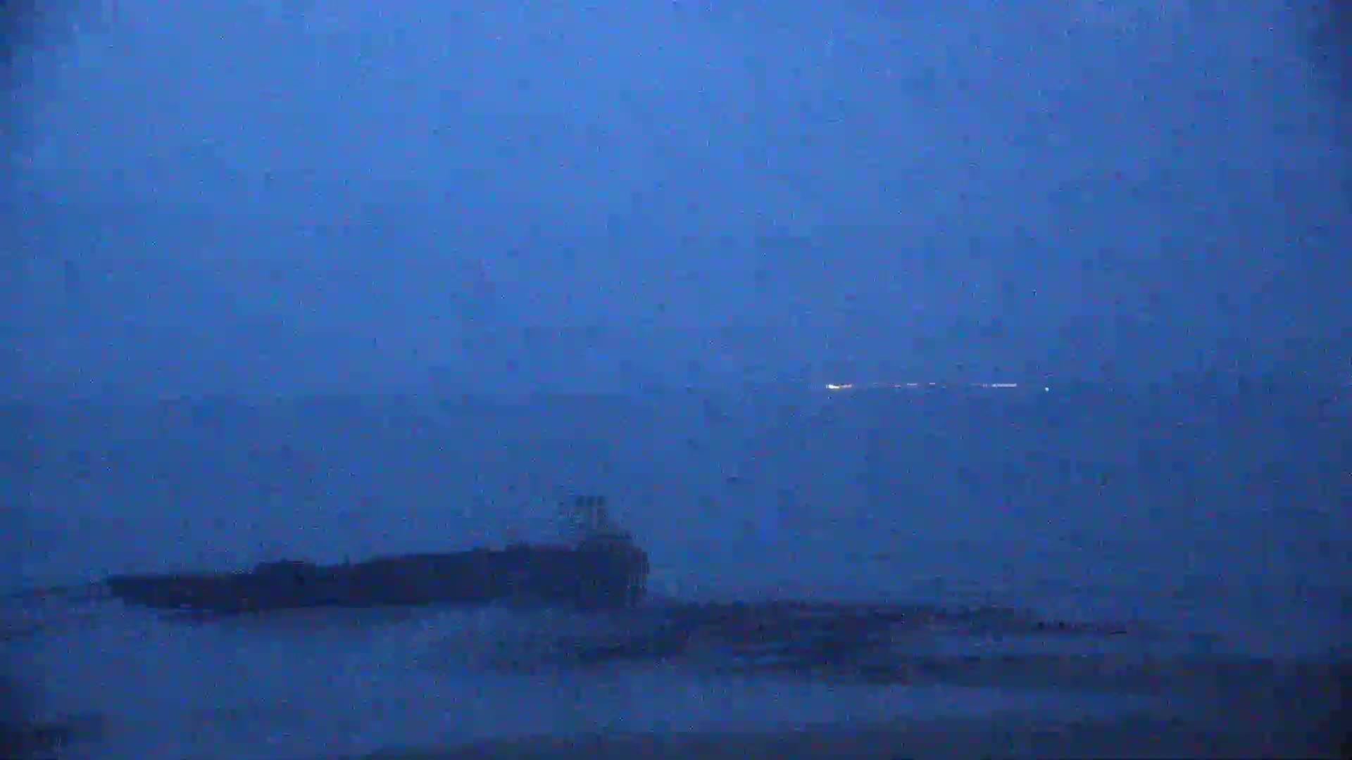 A dark structure sits on a body of water under a stormy, dark blue sky.