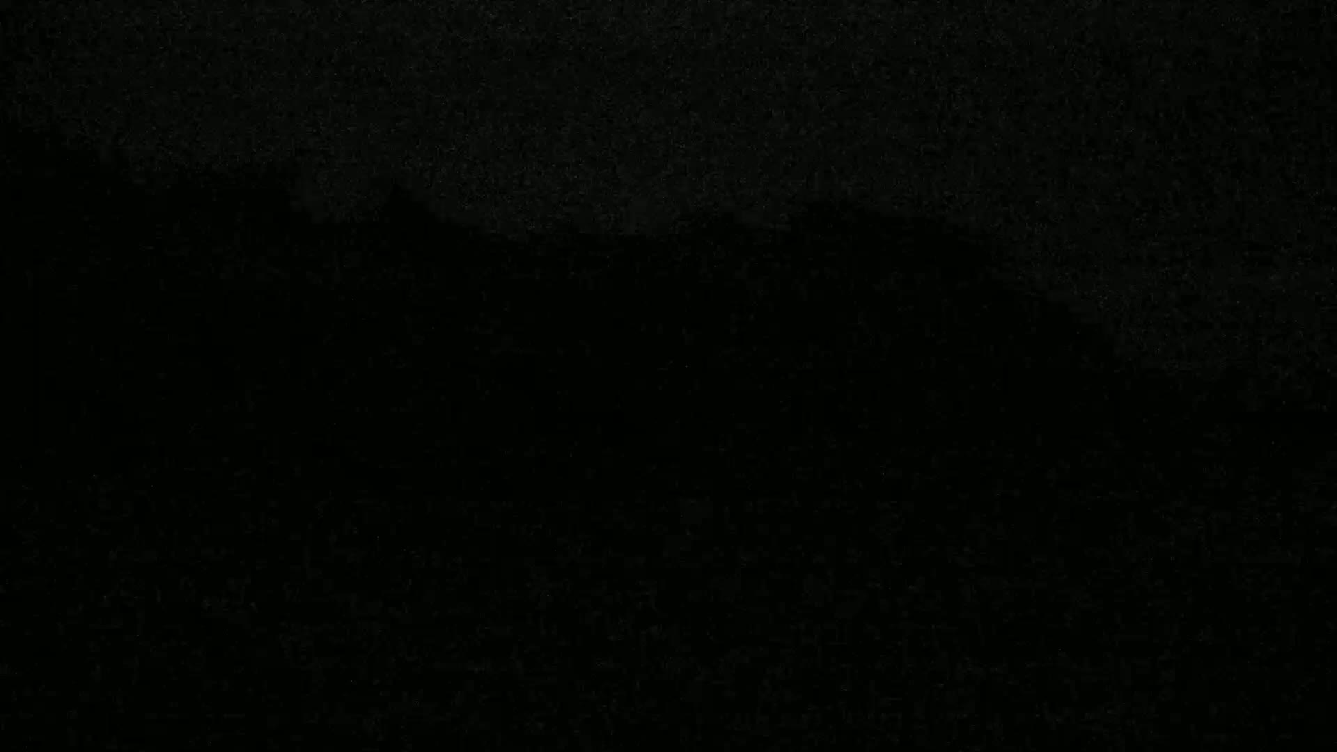 A dark, possibly nighttime, image shows a silhouetted mountain range against a very dark sky.