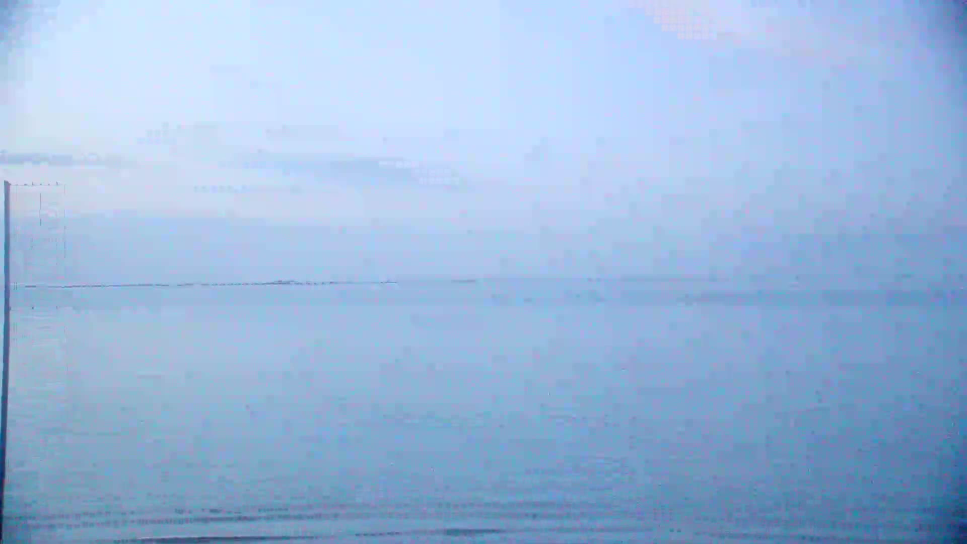 A hazy, light-blue ocean stretches to a pale horizon under a mostly clear sky.
