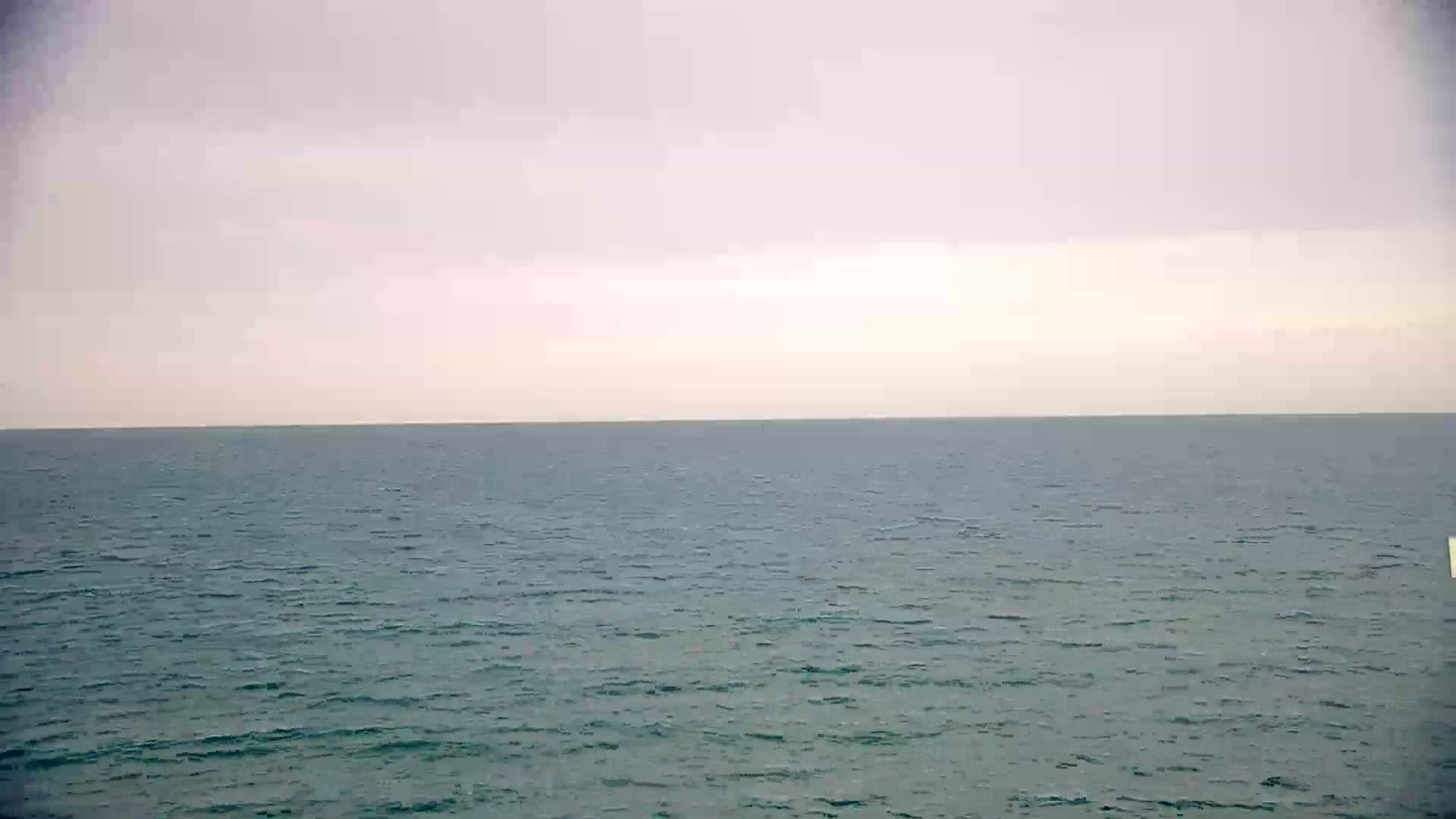 A calm, teal ocean stretches to a pale, overcast sky.