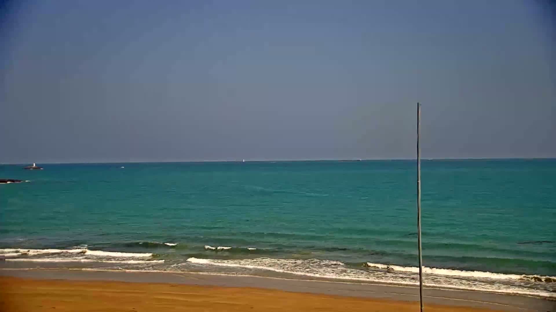A sandy beach meets a teal ocean with small waves under a clear blue sky.