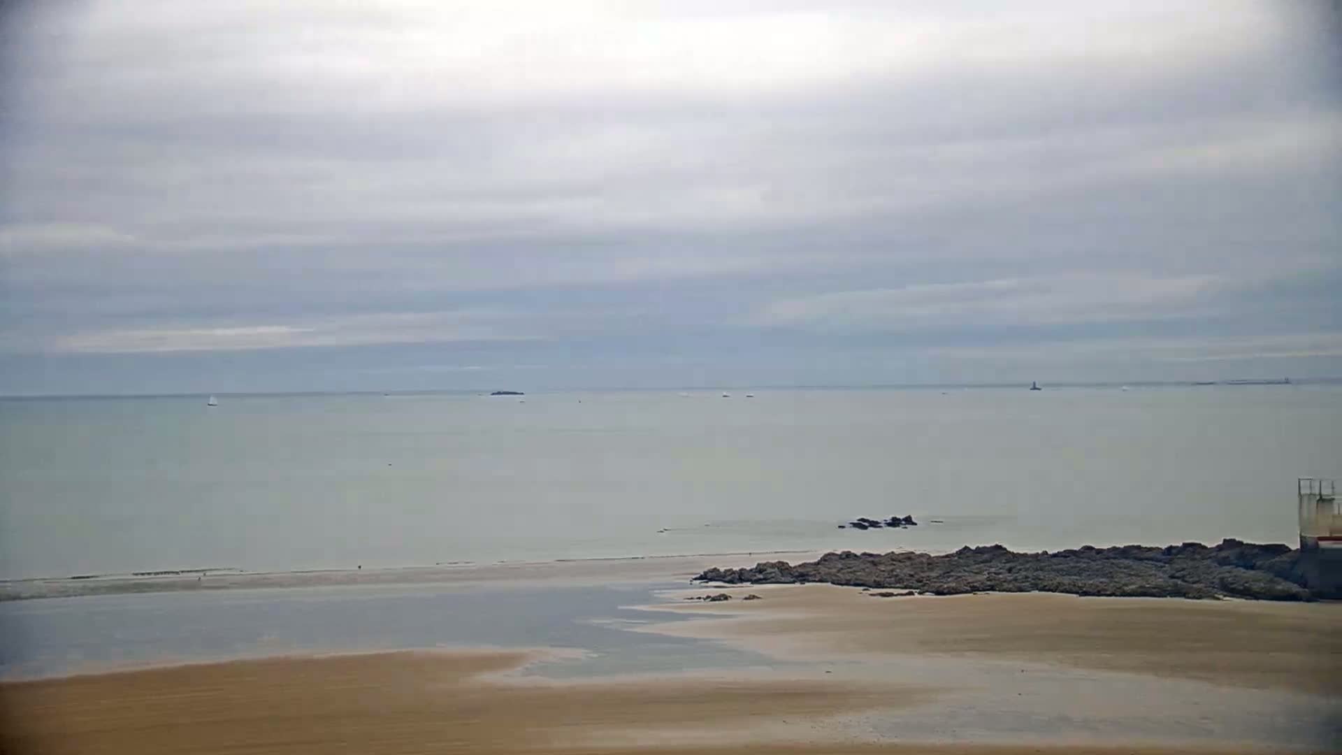 A sandy beach meets a calm, light-grey sea under a cloudy sky.