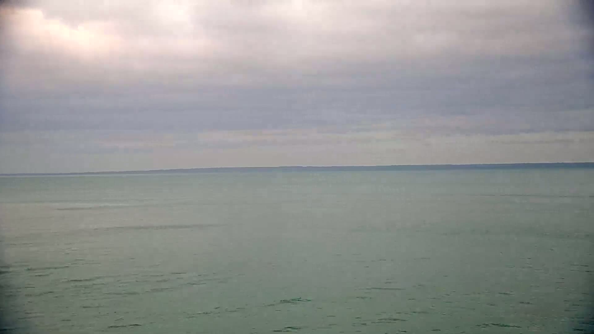 A calm, light-green body of water stretches to a dark horizon line under a cloudy sky.