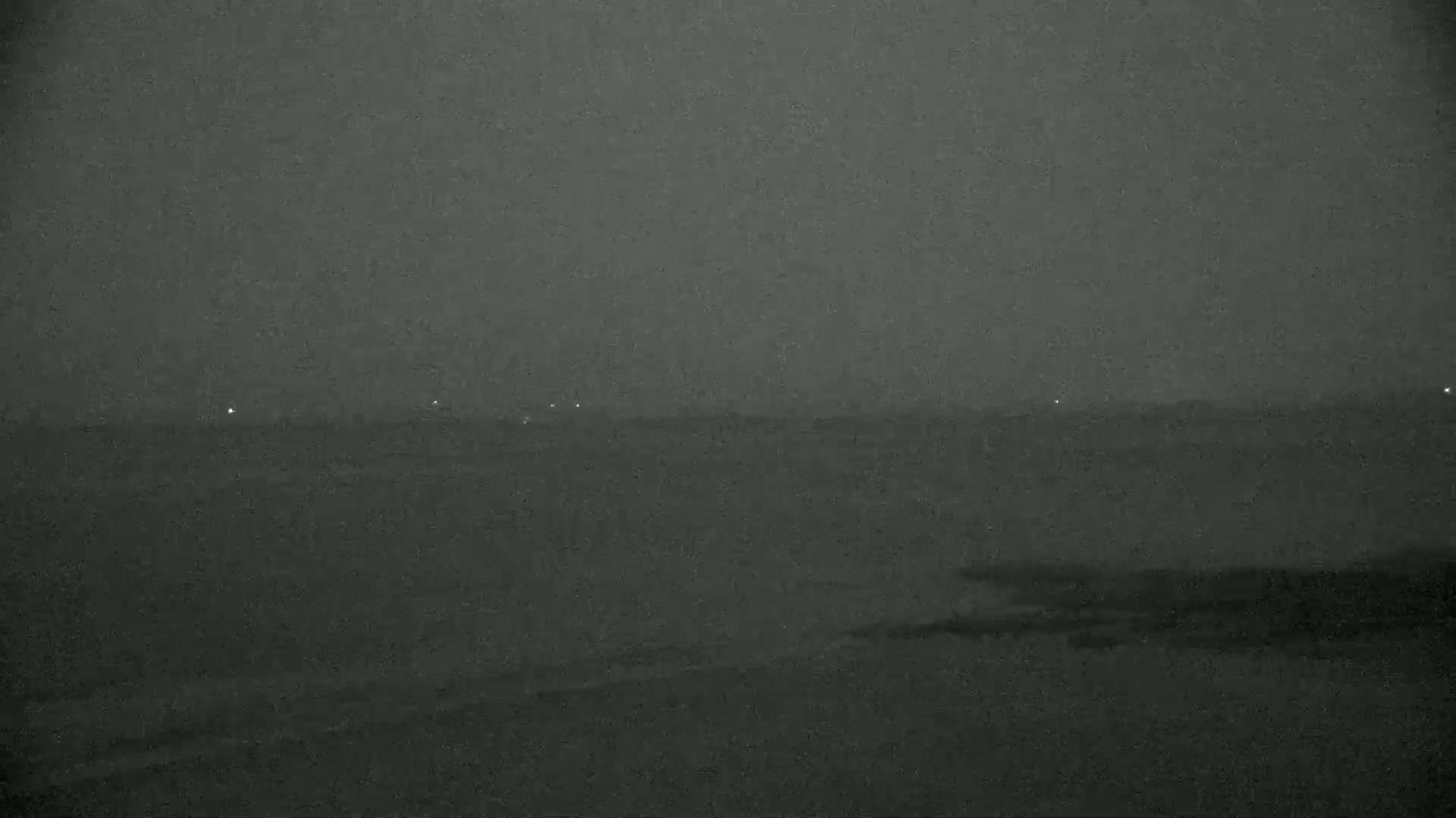 A dark, hazy landscape is visible at night, with a few faint lights in the distance.