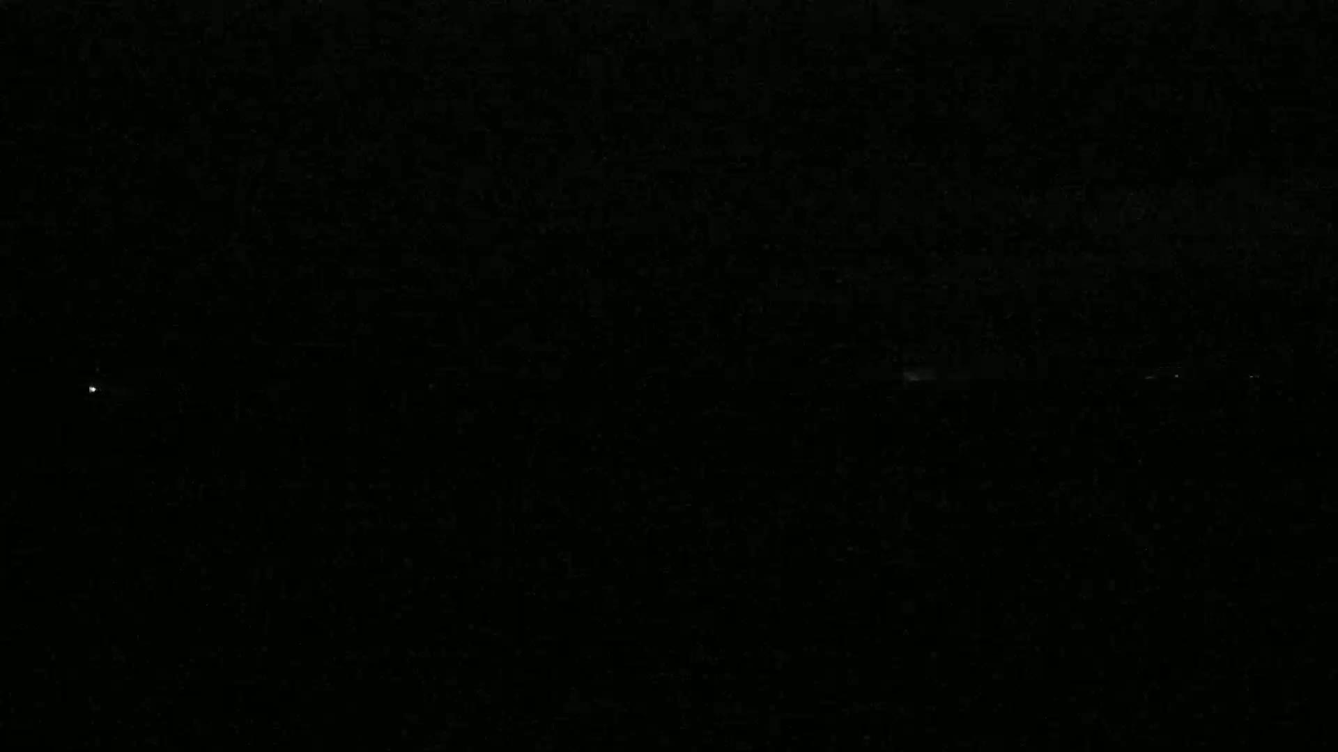 A mostly dark image shows a few faint lights on the horizon at night.