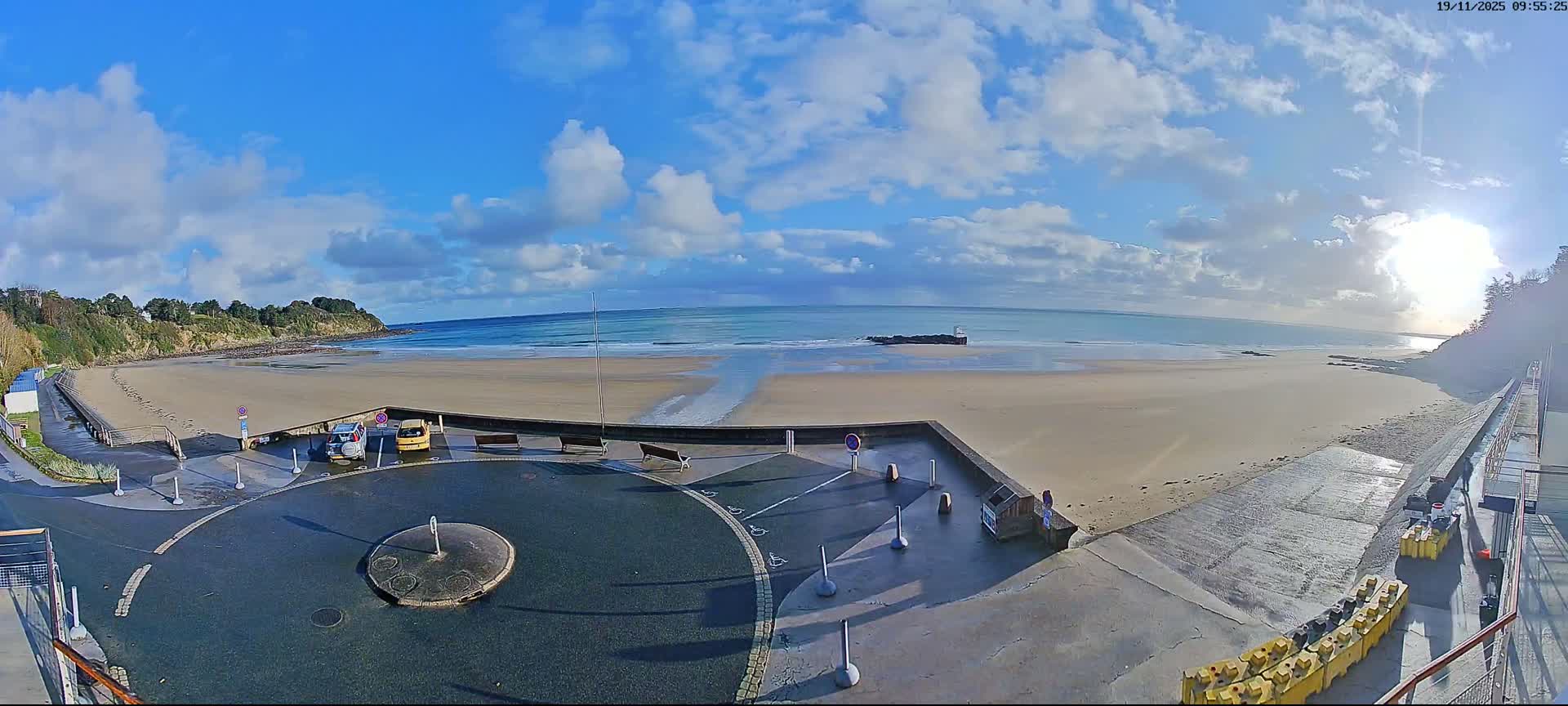 A calm, pale-blue sea meets a sandy beach under an overcast sky.