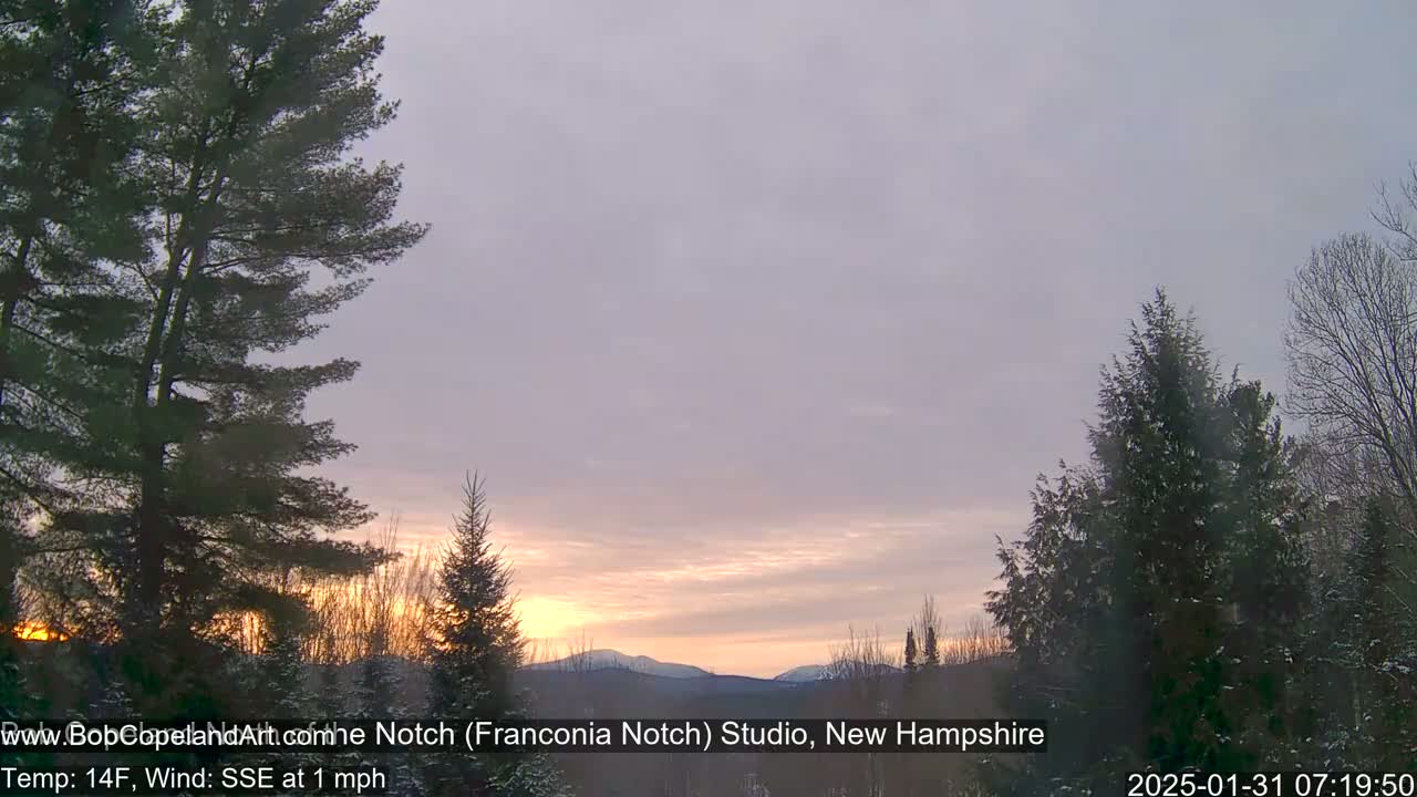 A sunrise casts a warm glow over snow-covered trees and distant mountains, with a light SSE wind at 1 mph and a temperature of 14°F.
