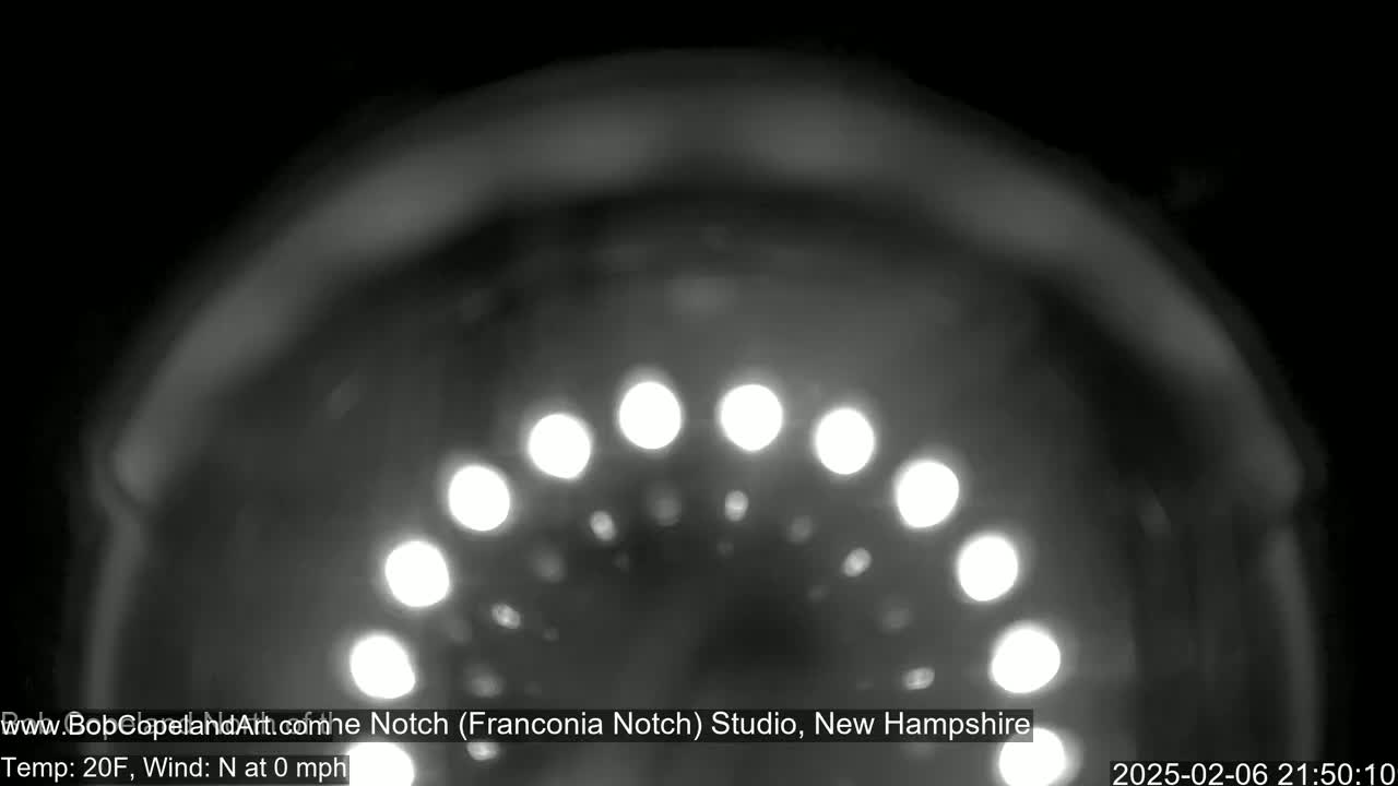A blurry, nighttime grayscale image shows a curved arrangement of out-of-focus lights against a dark background in 20-degree Fahrenheit weather with no wind.