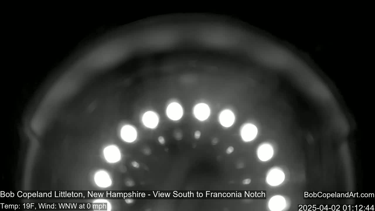 A nighttime, blurry image shows a semi-circular arrangement of bright lights against a dark, indistinct background in a 19°F temperature with a calm wind.
