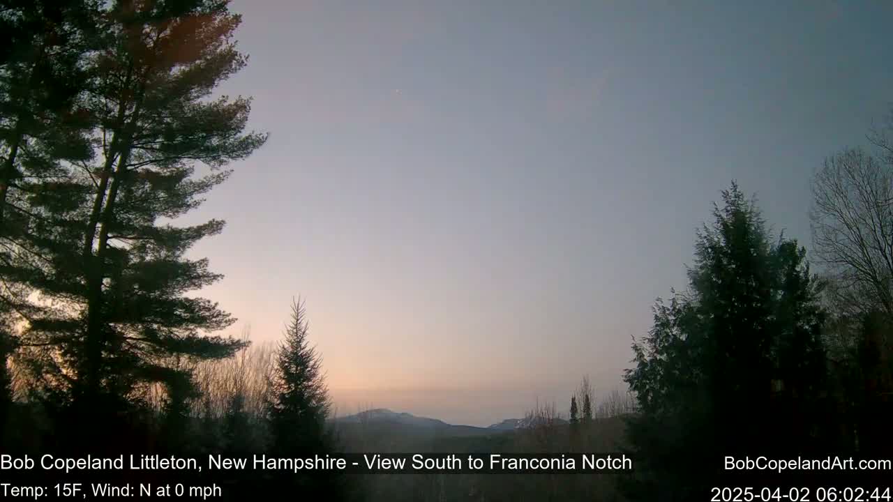 A pre-dawn, calm scene with a 15-degree temperature shows a view of distant mountains through a stand of dark evergreen trees.