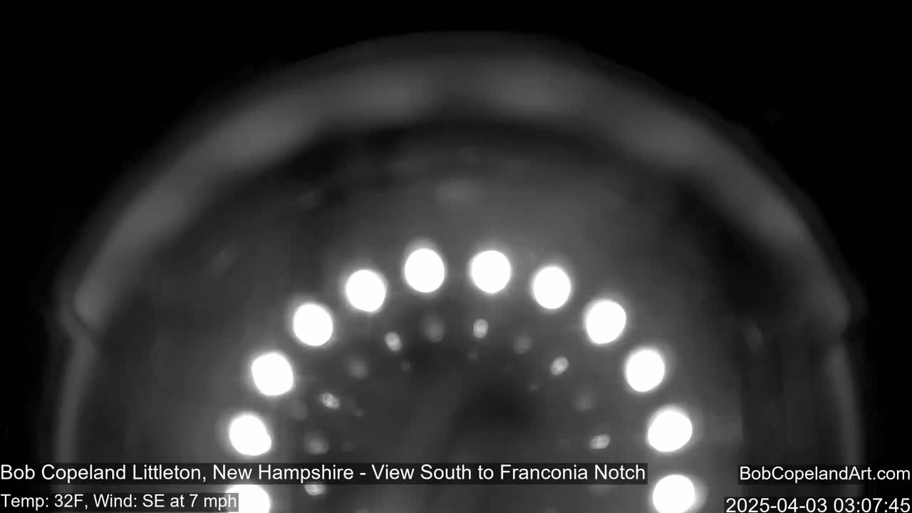 A blurry, nighttime image shows a curved array of bright lights against a dark background, with a southeasterly wind at 7 mph and a temperature of 32°F.