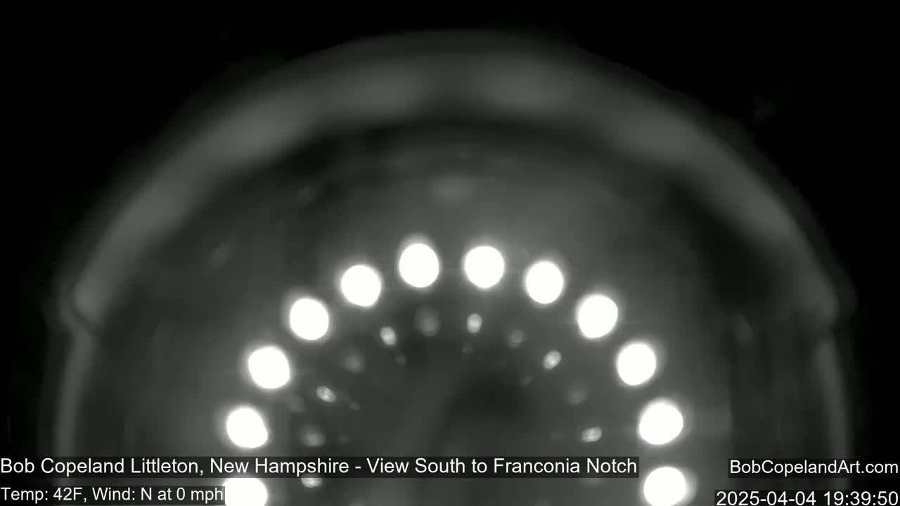 A blurry, nighttime image shows a semi-circular arc of bright lights against a dark background, with a temperature of 42°F and no wind.