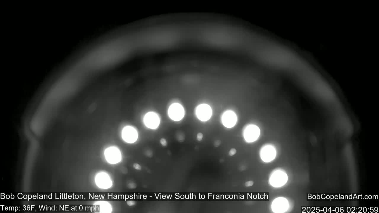 A nighttime, blurry image shows a semicircle of bright lights against a dark background, with calm weather conditions.