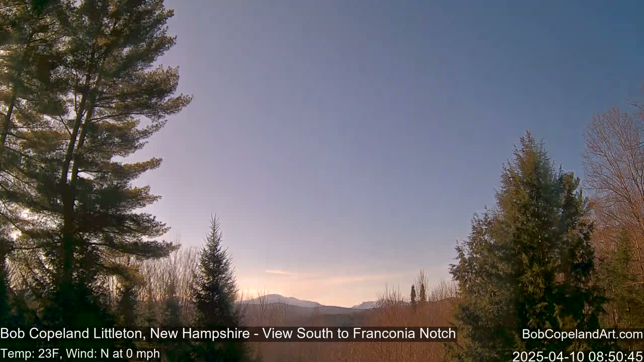 A clear, cold sunrise illuminates a mountainous landscape viewed from between evergreen trees.