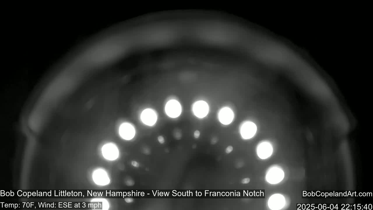 A blurry, nighttime image shows a semi-circular arrangement of bright lights, with a 70°F temperature and a 3 mph east-southeast wind.