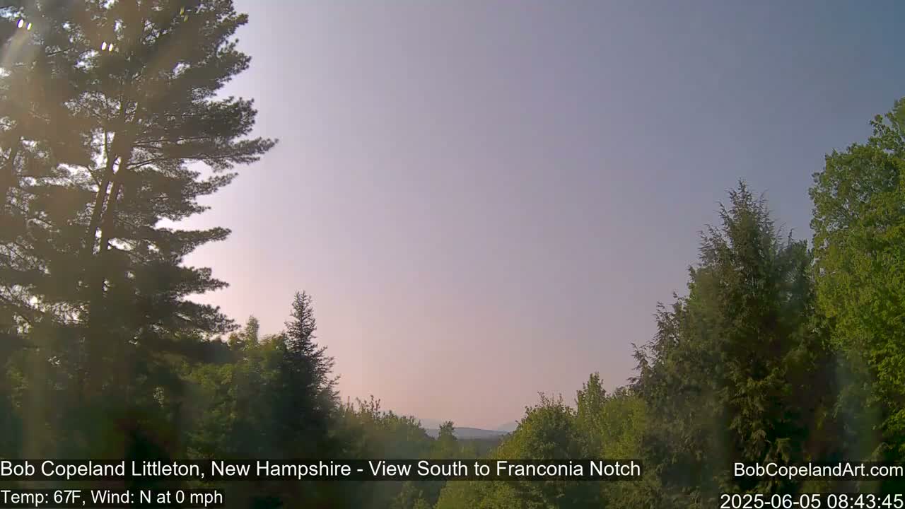 A calm, clear dawn illuminates a landscape of green trees and distant hills.