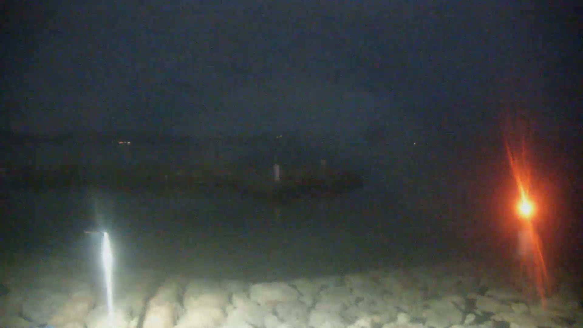 A dark, nighttime view of a body of water with a rocky shoreline, illuminated by two bright lights on either side of the frame.