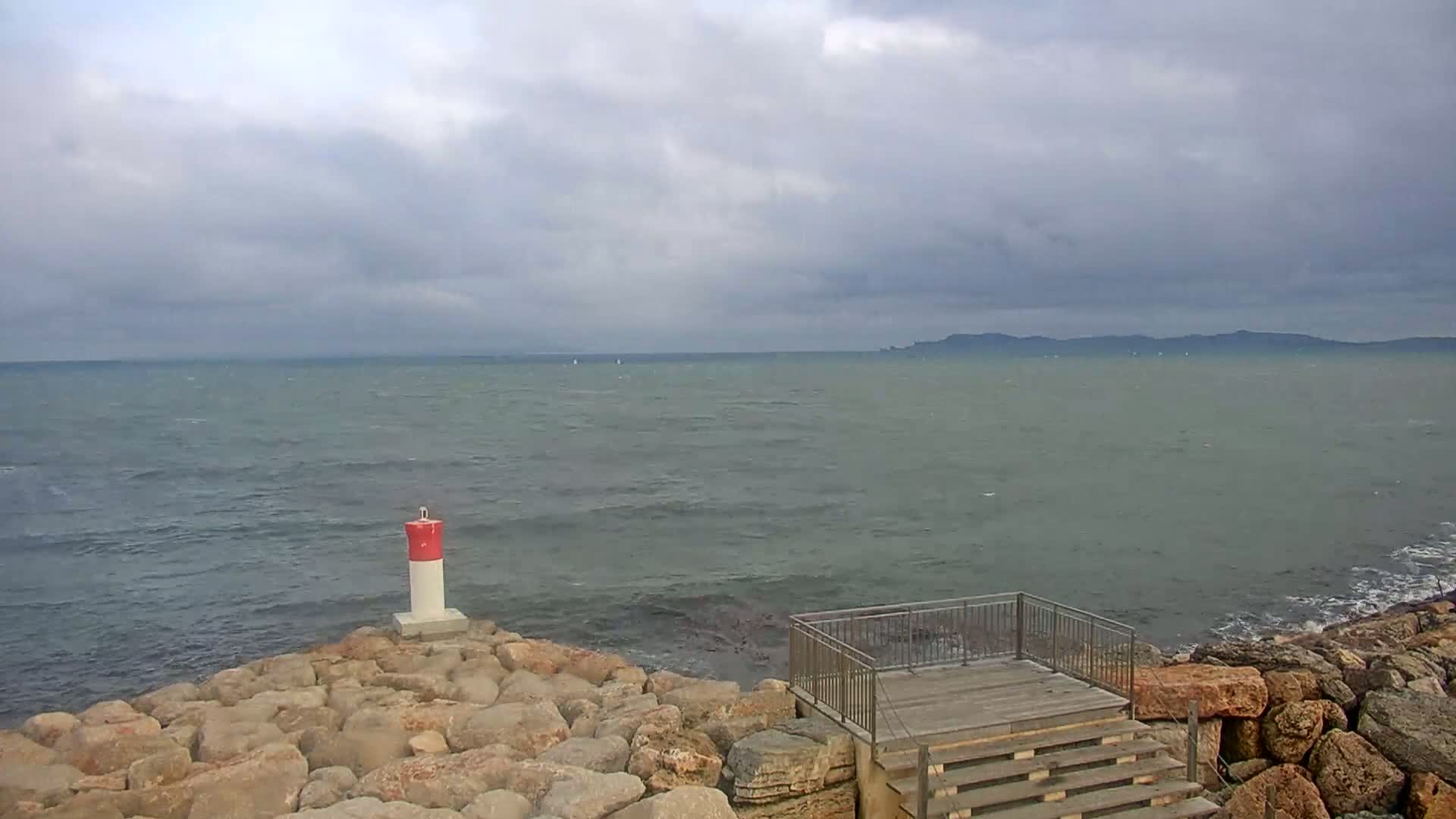 A rocky shoreline with a small wooden platform and stairs overlooks a choppy sea under a cloudy sky.