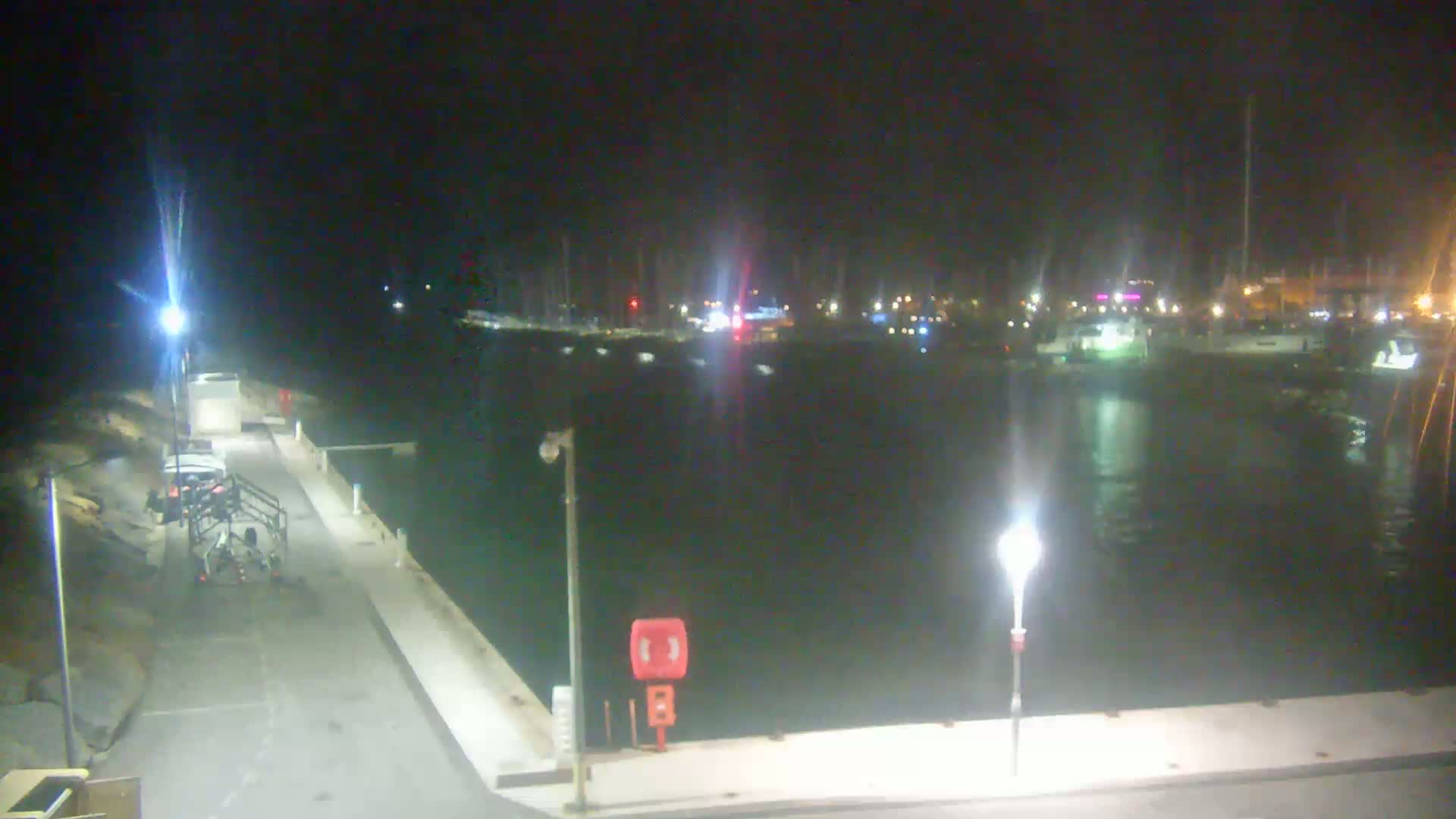 A nighttime view of a harbor filled with boats, lit by several lamps on a dock.