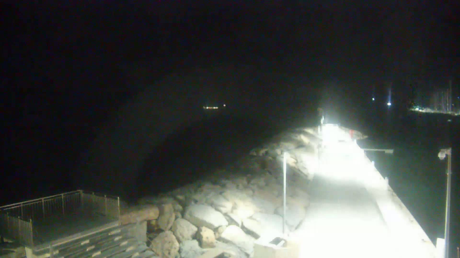 A brightly lit pier extends into dark water at night, with a rocky shoreline visible to one side.
